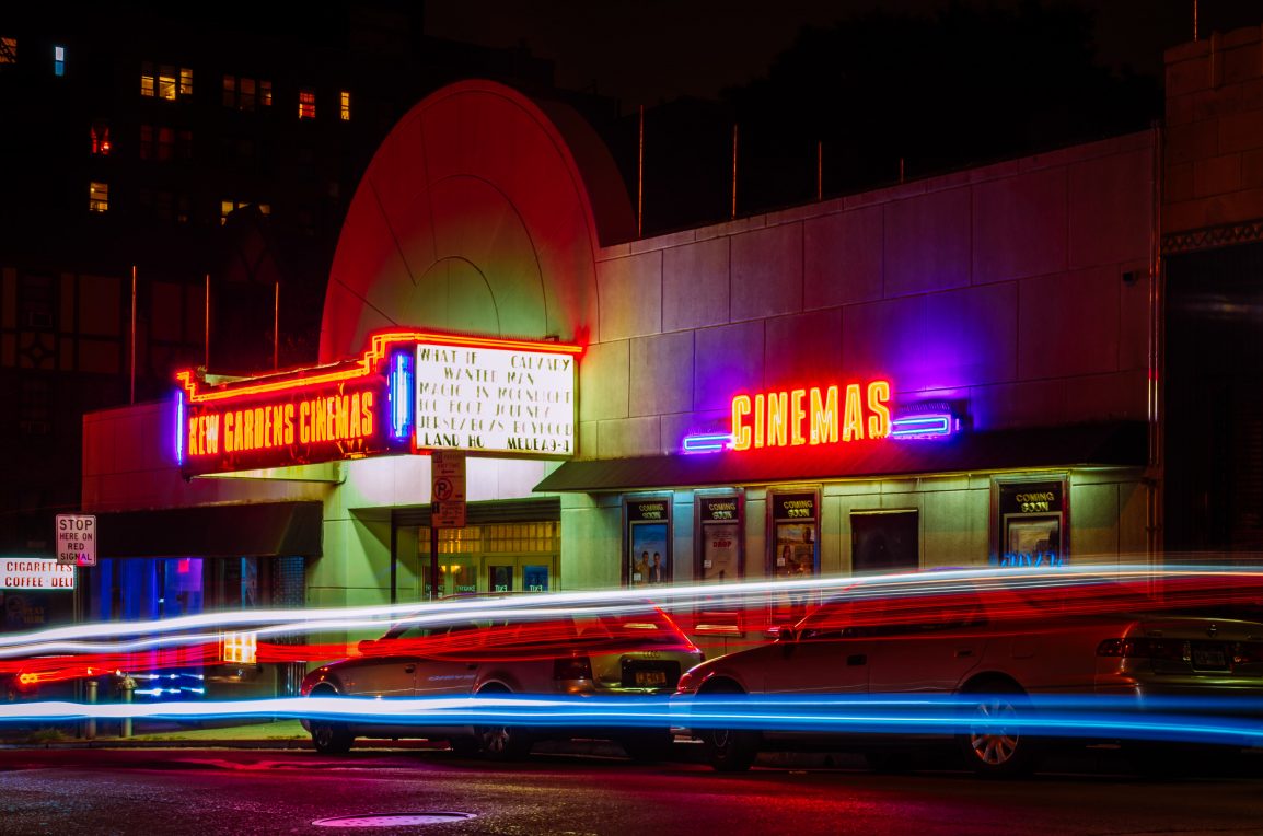 cars zoom by a cinema