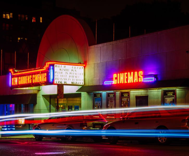 cars zoom by a cinema