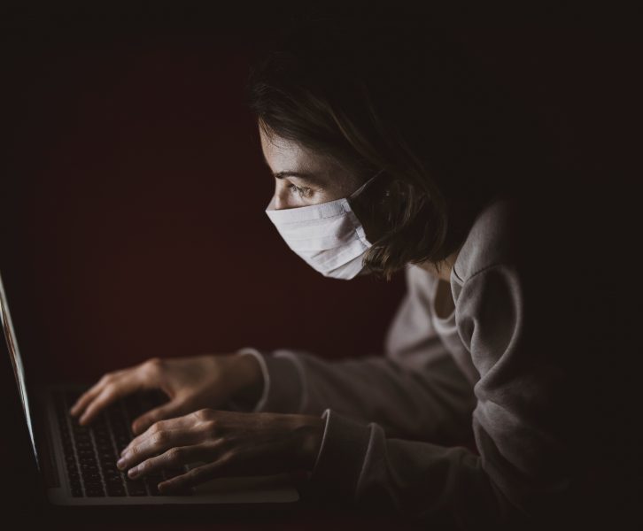 Person wearing mask and looking at a computer screen.