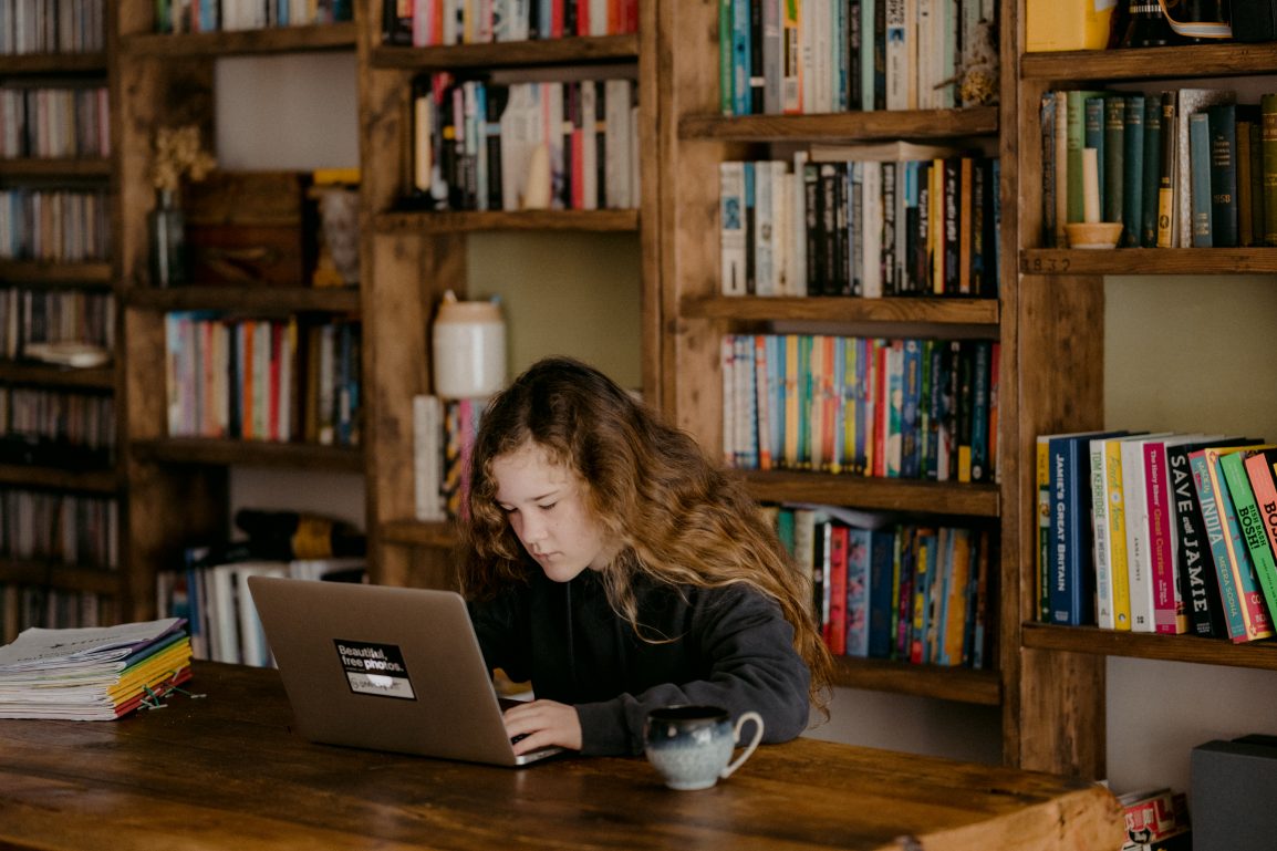 A girl looking at a computer in front of a bookshelf