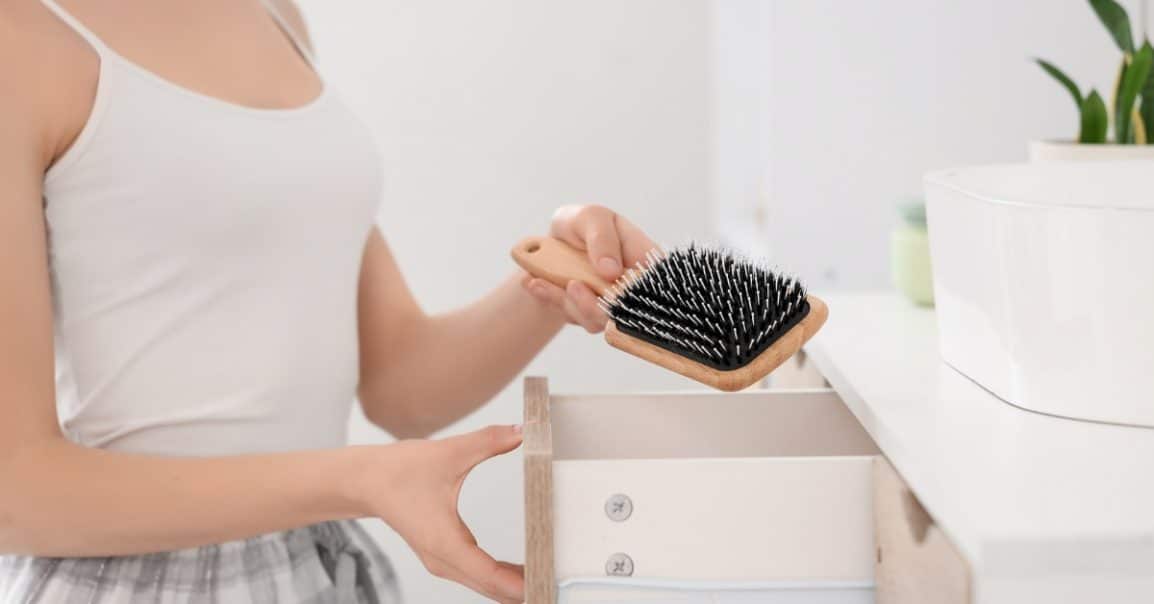 A girl places a clean hairbrush into a dresser drawer to keep everyday hair care tools organized and clean.