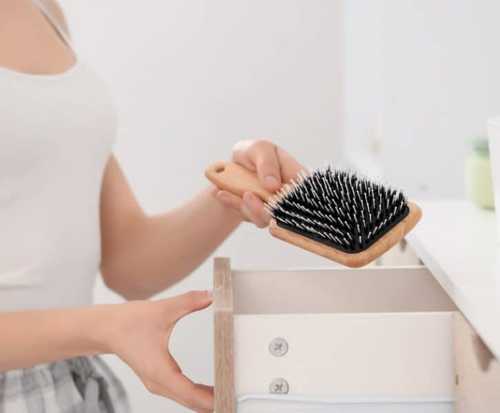 A girl places a clean hairbrush into a dresser drawer to keep everyday hair care tools organized and clean.