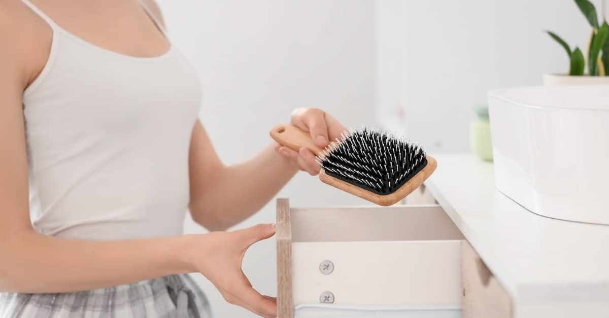 A girl places a clean hairbrush into a dresser drawer to keep everyday hair care tools organized and clean.